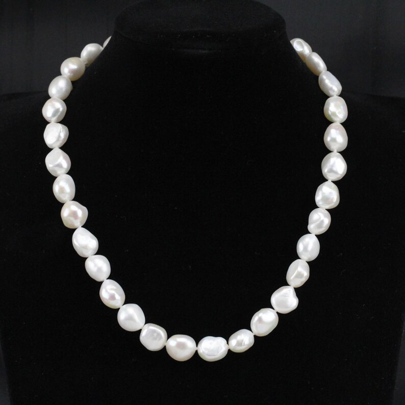 May include: A white pearl necklace with large, irregular shaped pearls. The necklace is on a black velvet background.