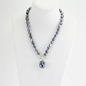 May include: A black freshwater pearl necklace with a large baroque pearl pendant. The necklace is made of a single strand of pearls and has a silver toggle clasp.