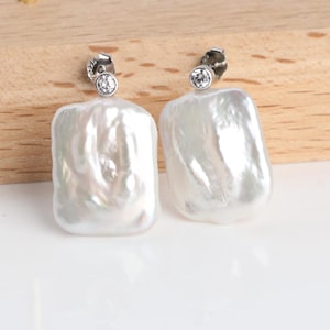 May include: A pair of white, baroque pearl earrings. Each earring features a large, irregular-shaped pearl with a shimmering surface. A small, round, clear crystal is set at the top of each earring.