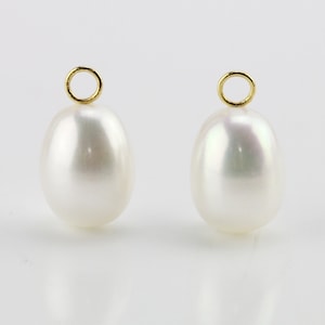 May include: Two white oval pearls with gold jump rings at the top. The pearls are smooth and have a slight iridescent sheen.