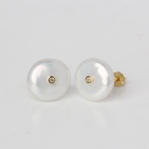 May include: A pair of white pearl earrings with a small diamond accent in the centre of each pearl.