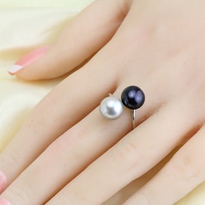 May include: A silver ring with a black pearl and a white pearl. The ring is designed to be worn on the middle finger.