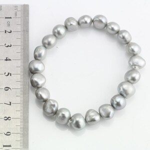 May include: A silver pearl bracelet with a ruler in the background. The pearls are approximately 1 cm in diameter.