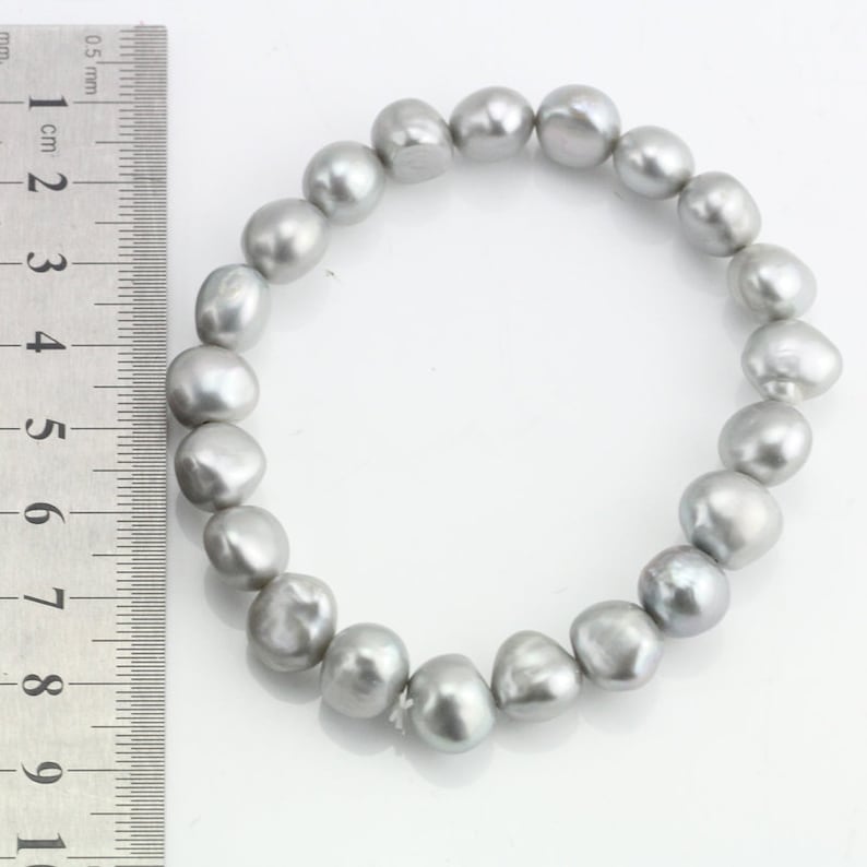 May include: A silver pearl bracelet with a ruler in the background. The pearls are approximately 1 cm in diameter.
