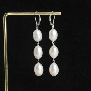 Puede incluir: Un par de pendientes de plata con tres perlas blancas en cada pendiente.