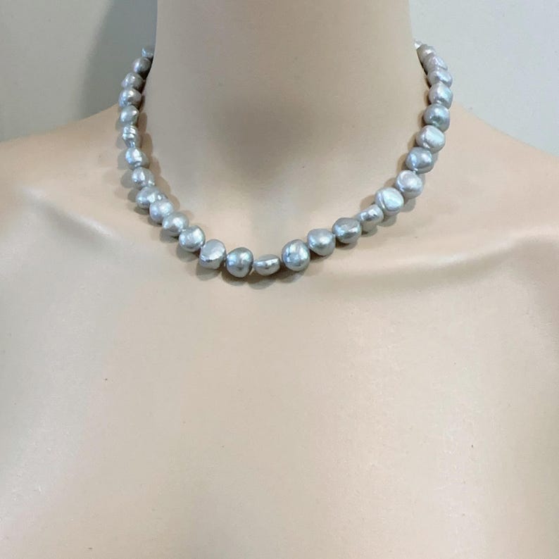 May include: A strand of gray freshwater pearls displayed on a mannequin. The pearls are irregularly shaped and have a subtle luster. The necklace is a choker style, resting close to the neck. The background is a neutral color.