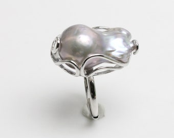 May include: A silver ring with a large, irregular, iridescent pearl set in a delicate, swirling wire design.