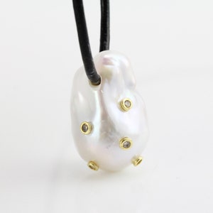 May include: A white baroque pearl pendant with small diamonds set in gold. The pearl is attached to a black leather cord.