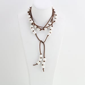 May include: A brown leather cord necklace with white pearl beads. The necklace is layered and has a long tassel.