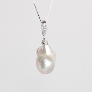 May include: A silver necklace featuring a large, irregularly shaped white pearl pendant. The pendant is attached to a silver bail set with small, clear gemstones. The pearl has a lustrous, iridescent sheen.
