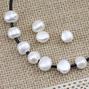 May include: A strand of white pearl beads on a black cord. The pearls are round and have a smooth, glossy finish.
