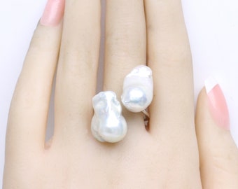 May include: A ring featuring two large, white baroque pearls. The pearls are irregular in shape and have a natural, organic look.
