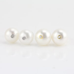 Puede incluir: Cuatro pendientes de perla con un pequeño acento de diamante en el centro de cada perla. Los pendientes están dispuestos en fila, con las perlas aumentando de tamaño de izquierda a derecha.