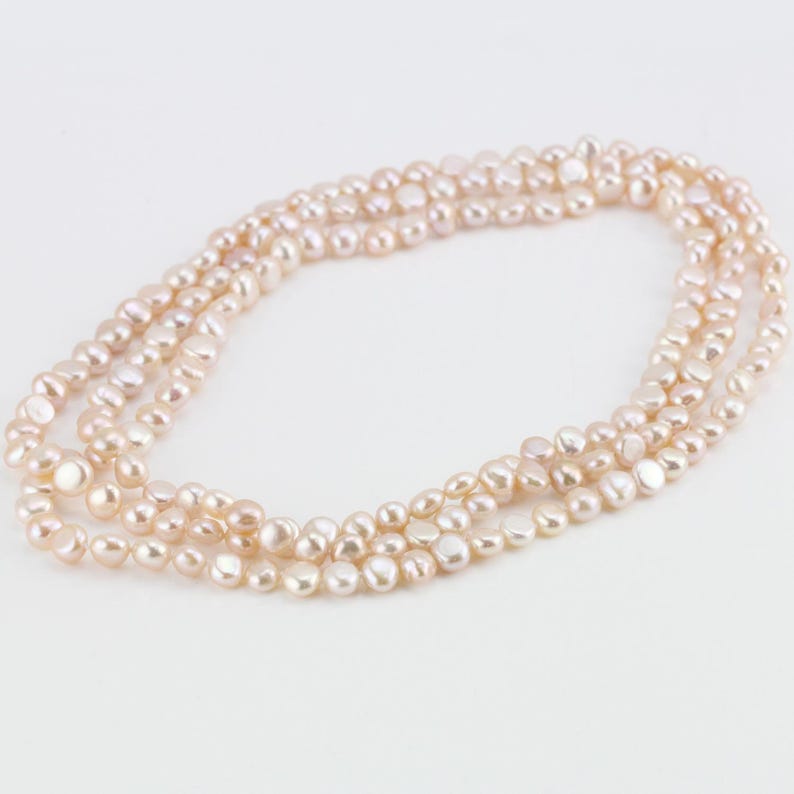 May include: A multi-strand necklace made of pale pink freshwater pearls. The pearls are irregular in shape and have a slightly iridescent sheen.