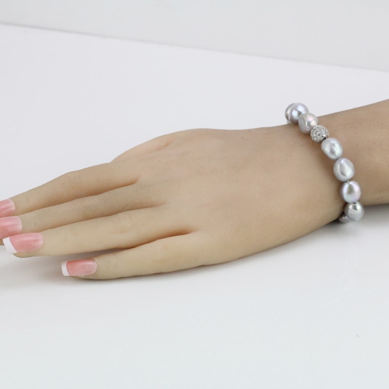 May include: A silver pearl bracelet with a small, sparkly, round charm in the center.