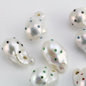 Pode incluir: Uma cole&ccedil;&atilde;o de p&eacute;rolas barrocas brancas com strass de diferentes cores. As p&eacute;rolas s&atilde;o de forma irregular e t&ecirc;m um furo perfurado. Algumas p&eacute;rolas t&ecirc;m strass pretos, outras t&ecirc;m strass azuis, outras t&ecirc;m strass verdes e outras t&ecirc;m strass vermelhos.