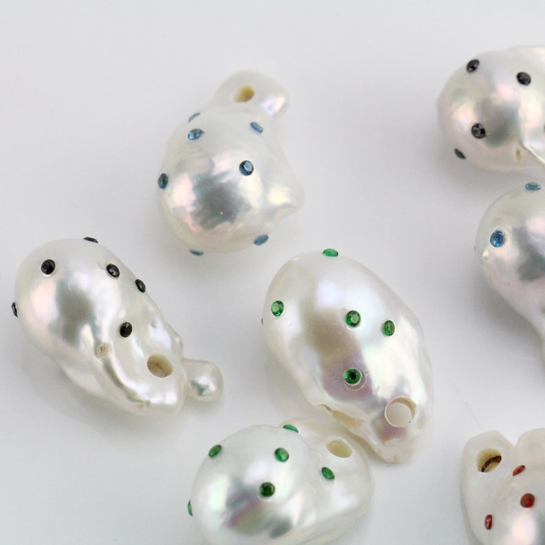 Pode incluir: Uma cole&ccedil;&atilde;o de p&eacute;rolas barrocas brancas com strass de diferentes cores. As p&eacute;rolas s&atilde;o de forma irregular e t&ecirc;m um furo perfurado. Algumas p&eacute;rolas t&ecirc;m strass pretos, outras t&ecirc;m strass azuis, outras t&ecirc;m strass verdes e outras t&ecirc;m strass vermelhos.
