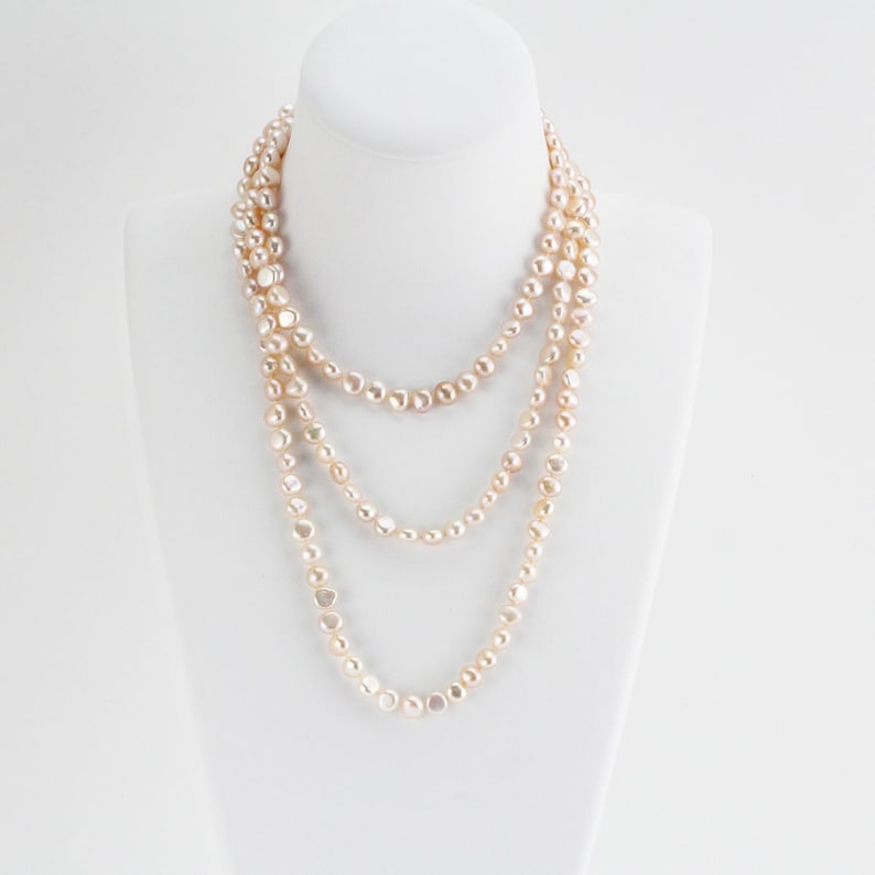 May include: A long, multi-strand necklace made of off-white pearls. The pearls are slightly irregular in shape and have a subtle sheen.