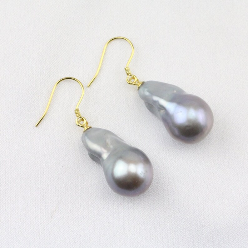 May include: A pair of silver baroque pearl earrings with gold hooks. The pearls are irregular in shape and have a pearlescent sheen.