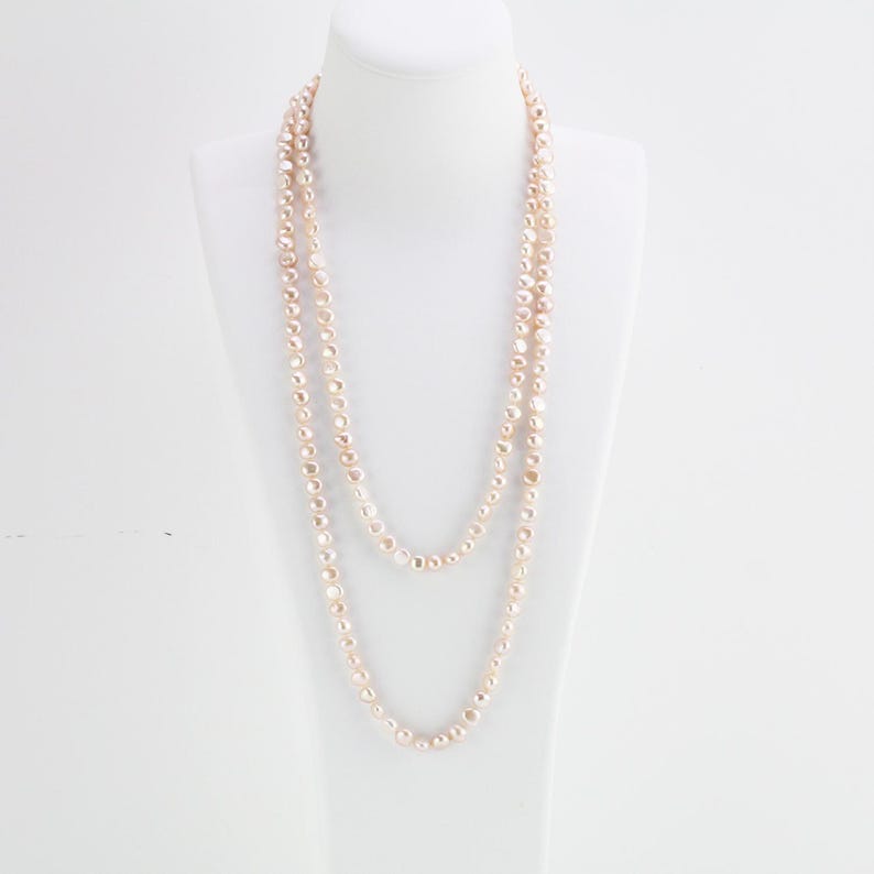 May include: A long, layered necklace made of small, round, cream-colored pearls.