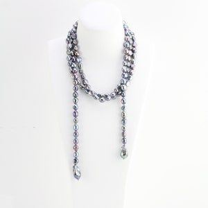 Puede incluir: Un collar largo y de varias capas hecho de perlas grises iridiscentes. El collar está enhebrado en un cordón delgado y tiene un borla al final.