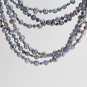 Puede incluir: Un collar de varias vueltas hecho de perlas barrocas de color gris oscuro. Las perlas son irregulares en forma y tamaño, y tienen un ligero brillo iridiscente.