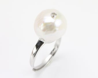 May include: A silver ring with a large white pearl and a small diamond set in the center.