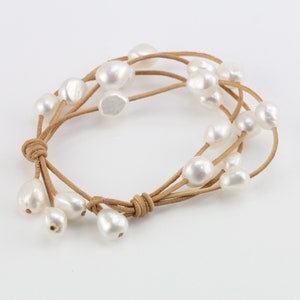 Könnte beinhalten: Ein mehrreihiges Lederarmband mit weißen Perlen. Das Armband ist mit einem Knoten gebunden und hat ein schlichtes Design.