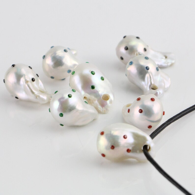 Pode incluir: Uma cole&ccedil;&atilde;o de p&eacute;rolas barrocas brancas com detalhes de pedras preciosas coloridas. As p&eacute;rolas s&atilde;o de forma irregular e t&ecirc;m um acabamento liso e brilhante. Algumas das p&eacute;rolas s&atilde;o enfiadas em um cord&atilde;o preto.