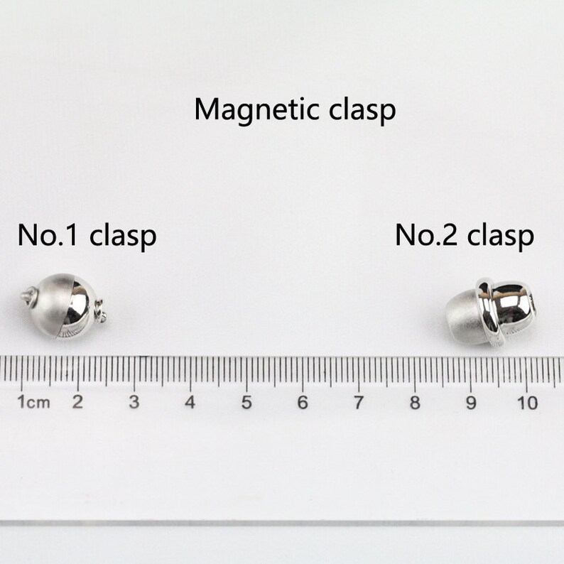 May include: Two silver magnetic clasps for jewelry making. The clasps are shown next to a ruler with measurements in centimeters. The first clasp is round and the second clasp is oval.