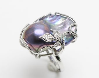 May include: A silver ring with a large, iridescent baroque pearl set in a delicate, leafy design. The pearl has a deep purple hue with hints of green and blue.
