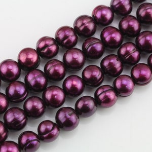 May include: A strand of deep purple freshwater pearls. The pearls are round and have a smooth, glossy finish.