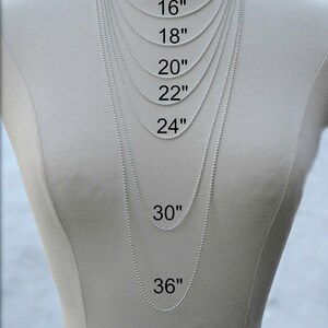 May include: A white mannequin wearing a silver chain necklace in various lengths, from 14 inches to 36 inches. The necklace lengths are labeled in inches. The image shows how different necklace lengths look when worn.