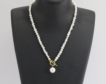 May include: A white pearl necklace with a gold toggle clasp and a single large pearl pendant.