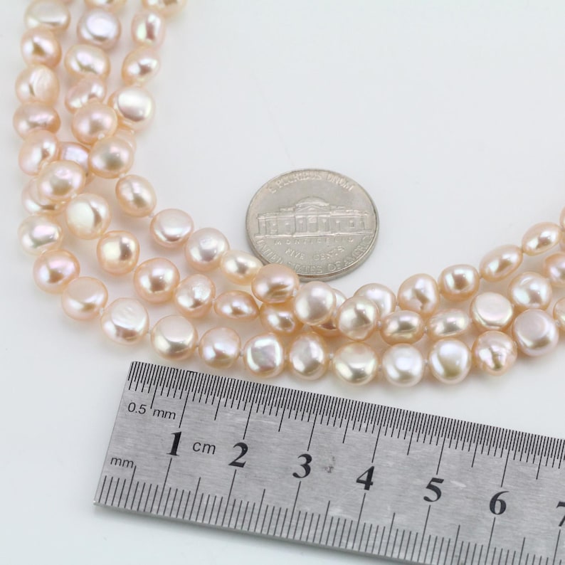 May include: A strand of pink freshwater pearls, measuring approximately 1 cm in diameter, with a ruler for scale.