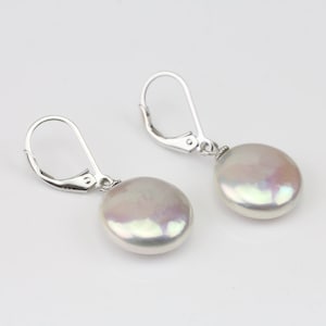 May include: A pair of silver dangle earrings with a round, white pearl drop. The pearls have an iridescent sheen.