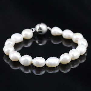 May include: A white pearl bracelet with a silver magnetic clasp. The pearls are oval shaped and have a smooth, glossy finish.
