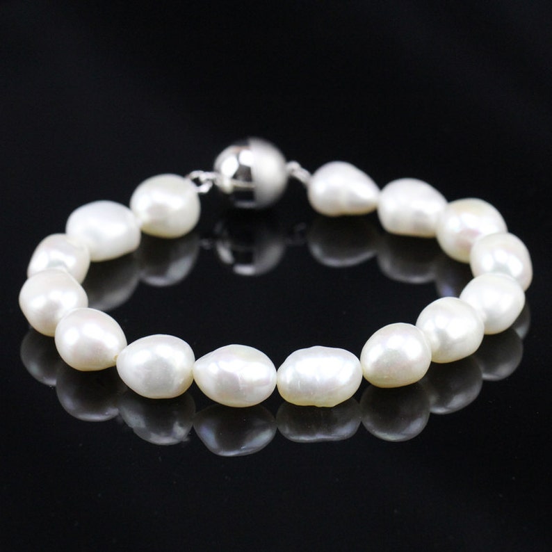 May include: A white pearl bracelet with a silver magnetic clasp. The pearls are oval shaped and have a smooth, glossy finish.