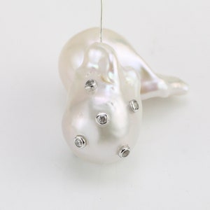 May include: A large, white baroque pearl with five small, clear rhinestones set into the surface.