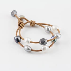 May include: A brown leather bracelet with a double strand of pearls. The pearls are in shades of white, gray, and black.