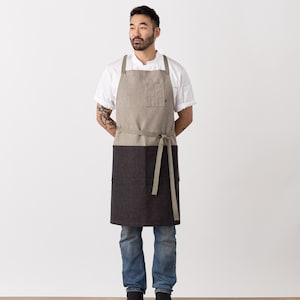 Puede incluir: Una persona que lleva una camisa blanca y un delantal marrón y negro con una correa verde. El delantal tiene un bolsillo en la parte delantera.