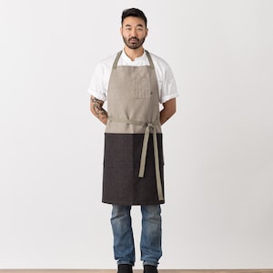 May include: A person wearing a white shirt and a brown and black apron with a green strap. The apron has a pocket on the front.