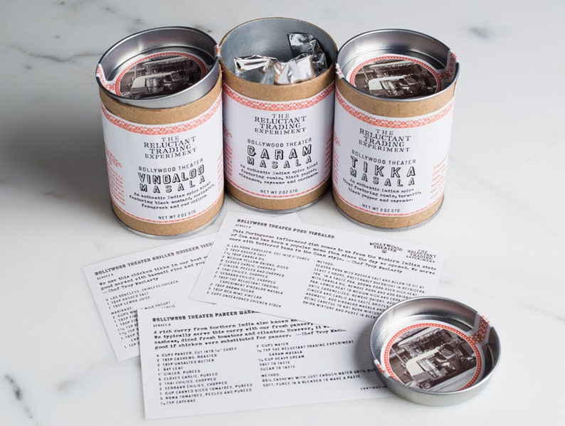 Puede incluir: Tres botes de metal con etiquetas marrones y texto blanco. Las etiquetas dicen "The Reluctant Trading Experiment" y "Bollywood Theater" seguidas de los nombres de diferentes mezclas de especias indias: "Vindaloo Masala", "Caram Masala" y "Tikka Masala". Cada bote tiene una peque&ntilde;a imagen de un coche antiguo en la etiqueta.