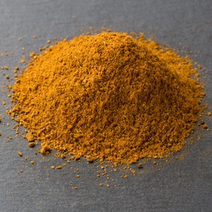 Puede incluir: Un mont&oacute;n de polvo de especias marr&oacute;n y naranja sobre una superficie gris oscura.