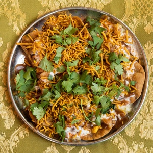 Puede incluir: Un plato de comida callejera india llamada dahi puri. El plato est&aacute; hecho con masa frita, patatas, garbanzos, yogur y especias. La comida est&aacute; adornada con cilantro y sev.