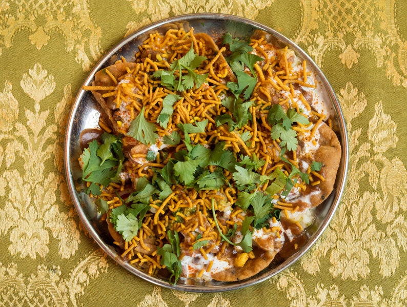 Puede incluir: Un plato de comida callejera india llamada dahi puri. El plato est&aacute; hecho con masa frita, patatas, garbanzos, yogur y especias. La comida est&aacute; adornada con cilantro y sev.