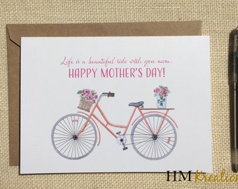 May include: A pink bicycle with a basket of flowers on the handlebars and a jar of flowers on the back rack. The card reads "Life is a beautiful ride with you mom. Happy Mother's Day!"