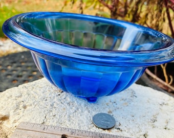 May include: A vibrant blue glass bowl with a fluted design. The bowl has a rounded shape with a wide rim and sits on three small feet. A ruler and a coin are next to the bowl.