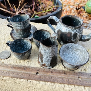 May include: A miniature ceramic tea set with a speckled blue and white glaze. The set includes a teapot, cups, saucers, a creamer, and a sugar bowl. The tea set is displayed on a light-colored surface.