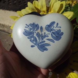 May include: A white heart-shaped ceramic trinket box with a blue floral design. The box is decorated with a stylized floral pattern in blue on a white background.
